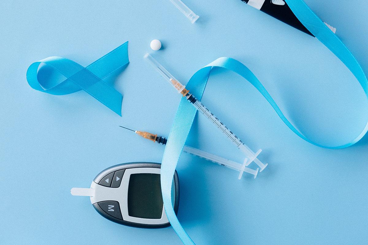 Máquina de medición de glicemia, jeringas de insulina y cinta celeste por la concientización de la Diabetes